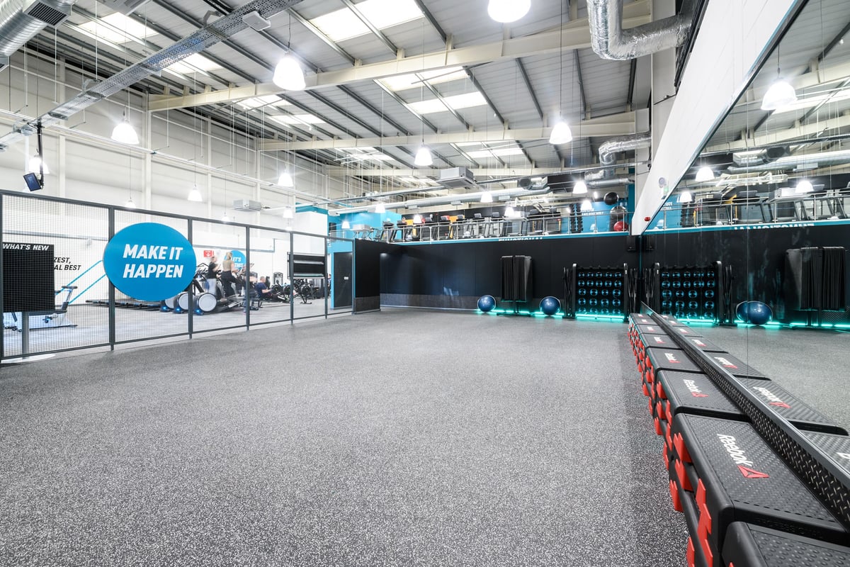 PureGym Folkestone: Large gym space with rubberized floors, weight racks, benches, and motivational signage on walls.