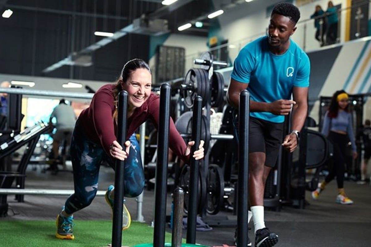 Lady pushing sled alongside personal trainer