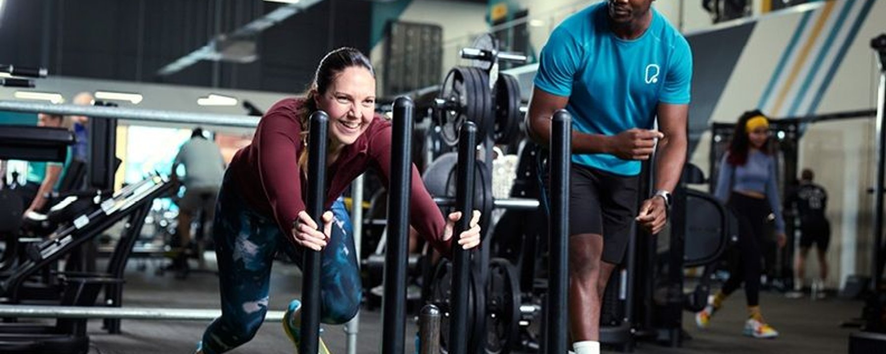 Lady pushing sled alongside personal trainer