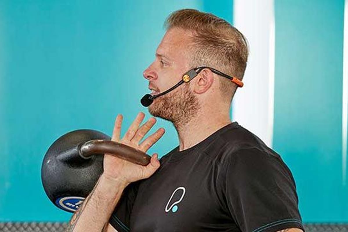 Homme avec casque soulevant un kettlebell dans une salle avec mur bleu