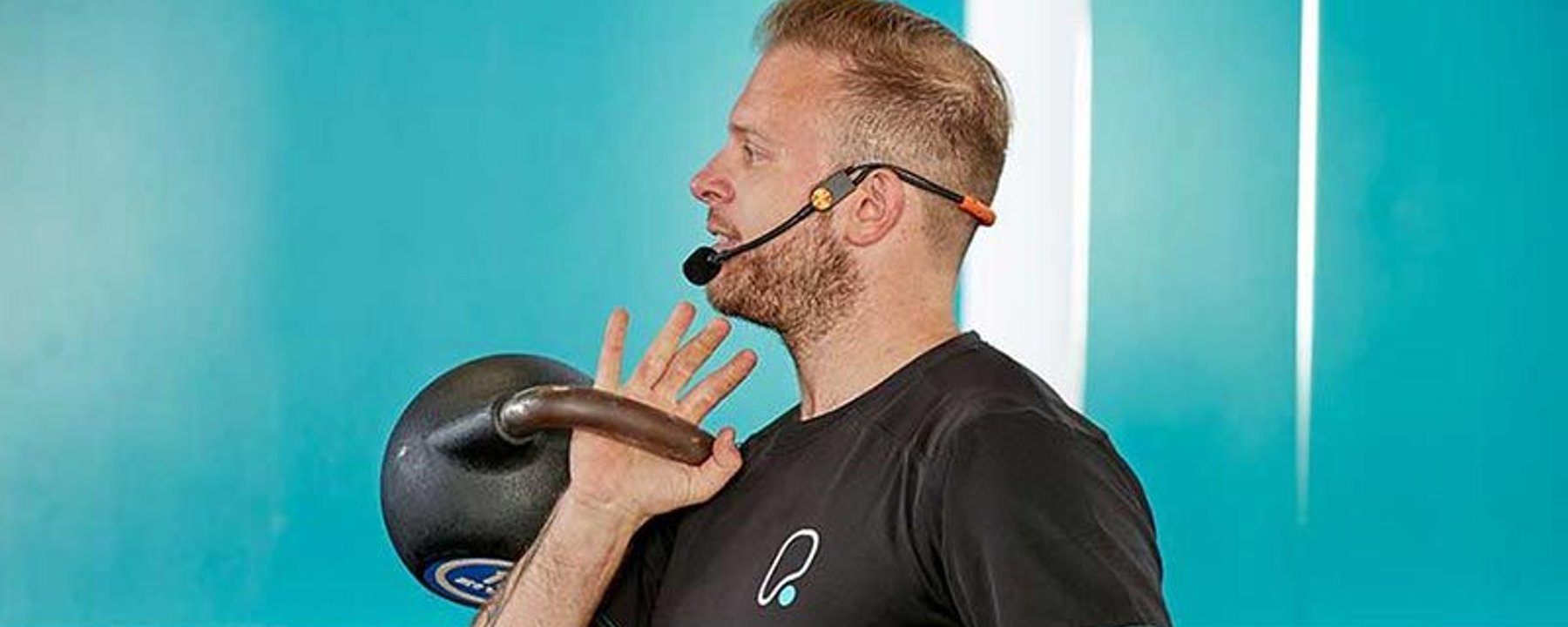 Homme avec casque soulevant un kettlebell dans une salle avec mur bleu