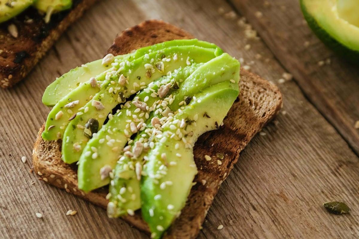 Sliced avocado on toasted whole grain bread sprinkled with seeds on wooden surface