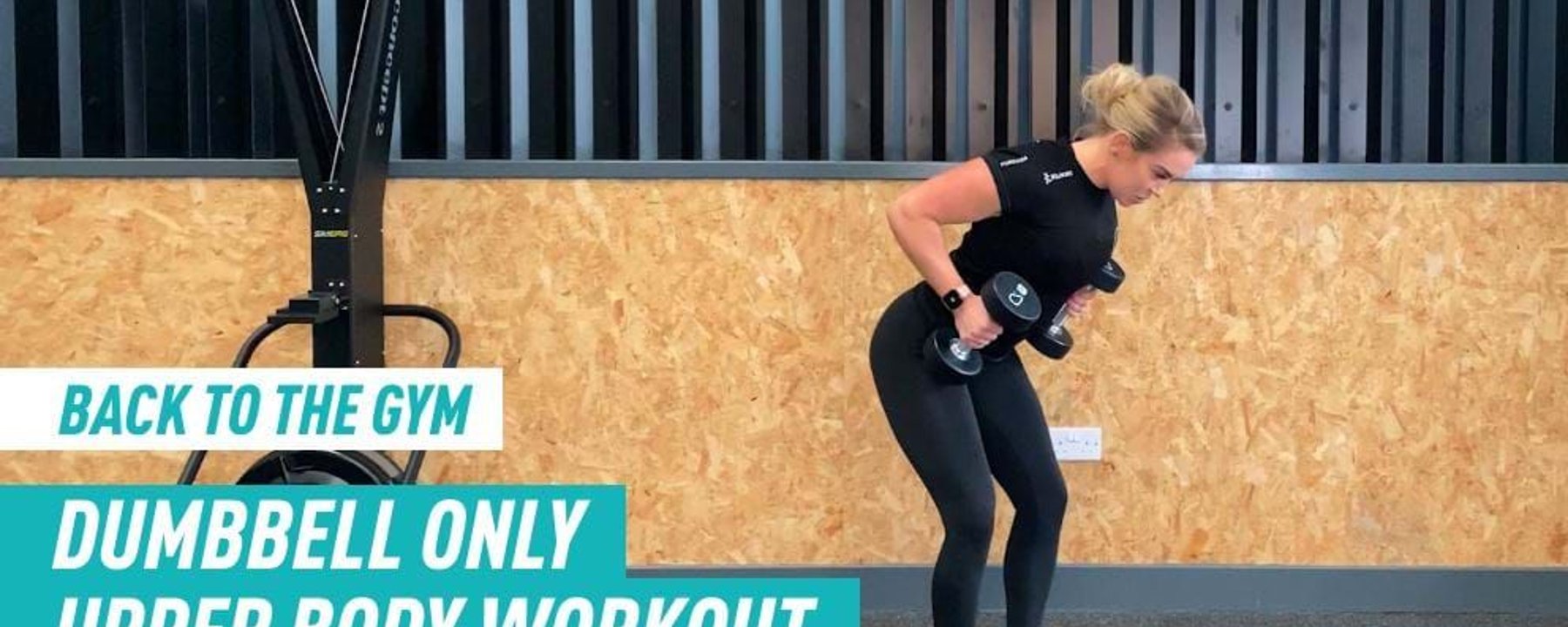 Woman in black workout clothes lifting dumbbells in gym with wooden wall background