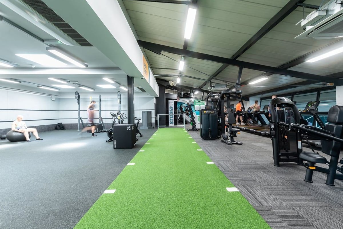PureGym London Bayswater: Weights, machines, green turf area for training, fans on ceiling in a well-equipped gym interior.