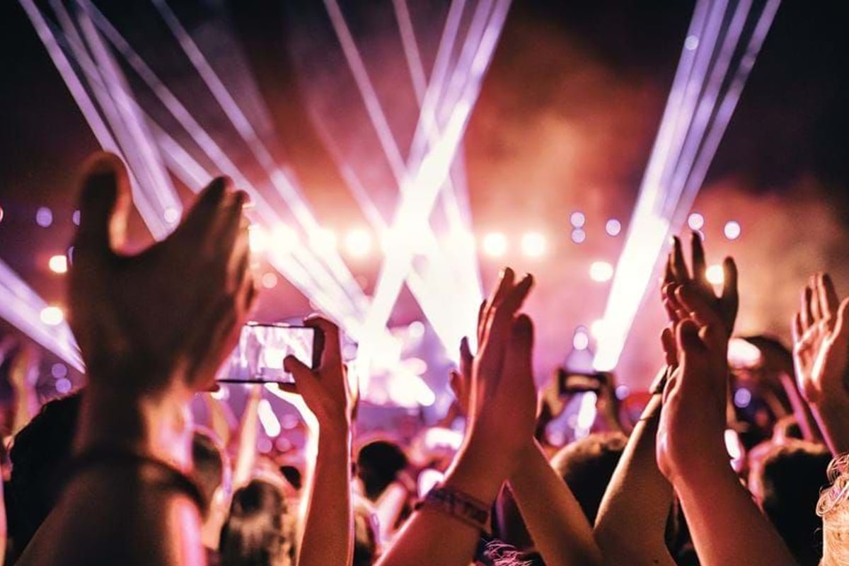 Crowd with raised hands and phones recording a brightly lit stage at night.