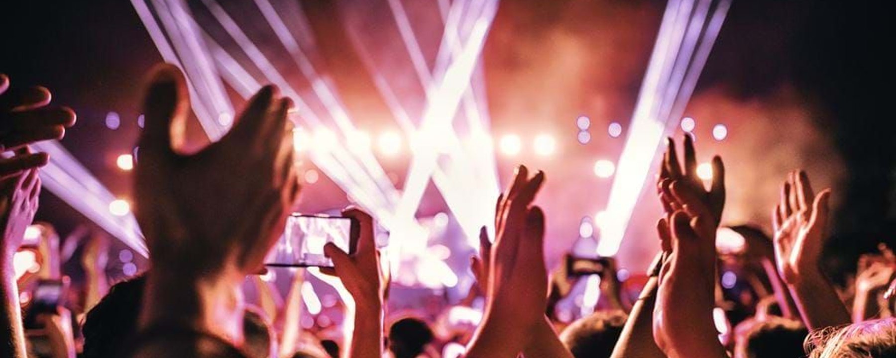 Crowd with raised hands and phones recording a brightly lit stage at night.