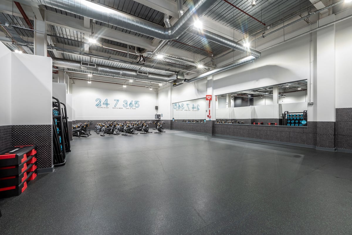 PureGym Newport Wales: Rows of cardio machines, rubberized flooring, exposed pipes and ducts on ceiling.