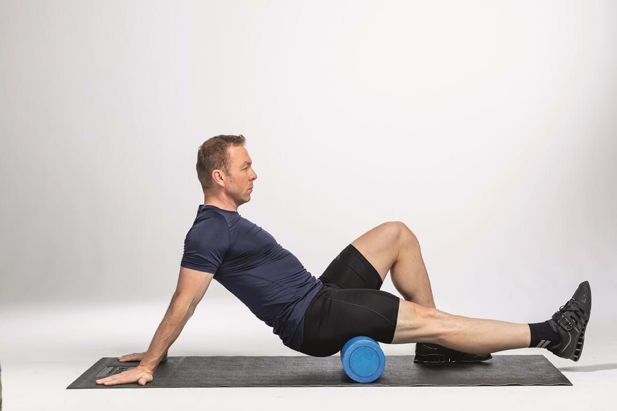 Man using a foam roller on his calf while sitting on a mat against a white background