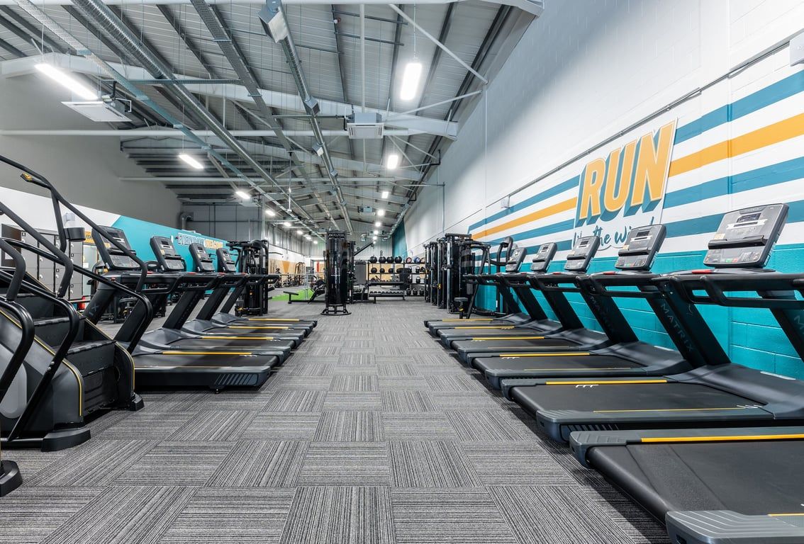 PureGym Byfleet: Rows of treadmills, bright lighting, and wall graphics featuring the word "RUN" in a gym setting.