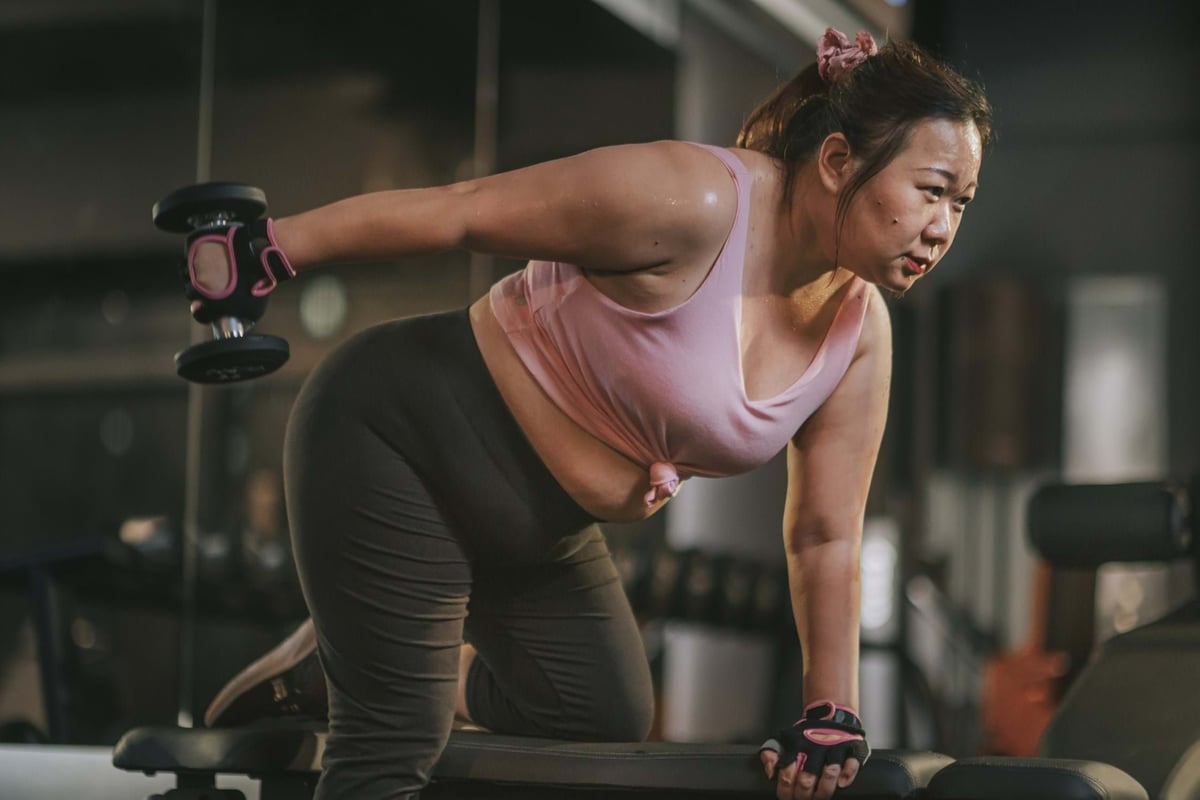 Woman lifting dumbbell in gym wearing pink top and black leggings