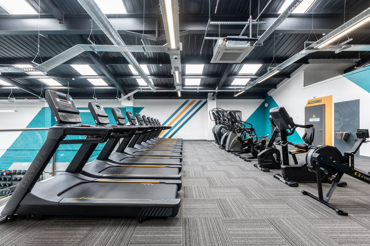 PureGym Dewsbury: Rows of treadmills, ellipticals, exercise bikes alongside weight machines in a modern gym setting.