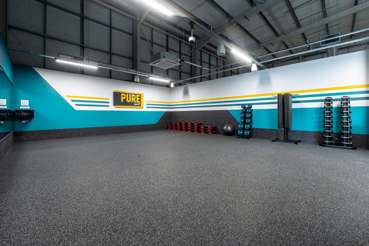 PureGym Sudbury: Strength training area with punching bag, dumbbell racks, rubberized flooring, and mirrored wall.