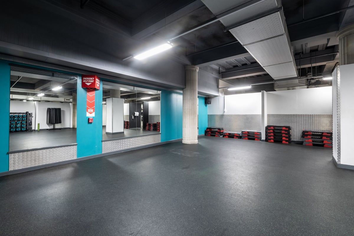 PureGym Liverpool Central: Weight racks, rubberised flooring, turquoise accents in basement gym setting.