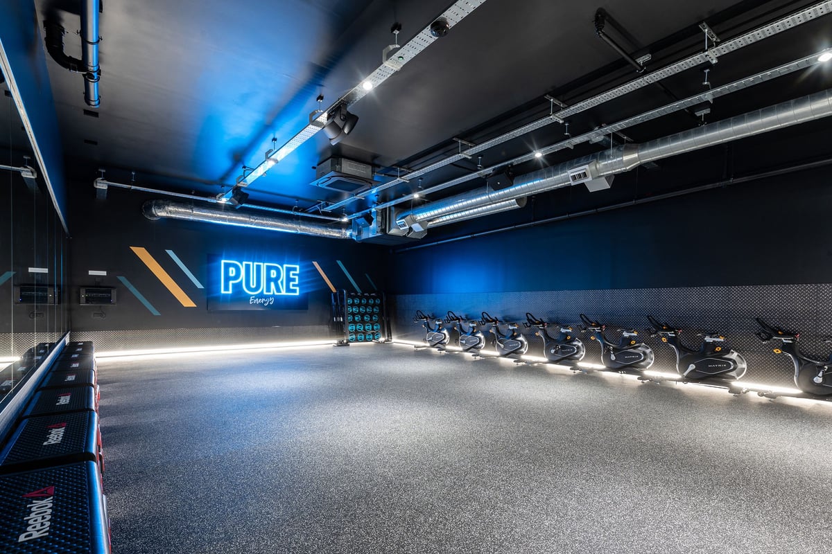 PureGym Portishead: Rows of spin bikes, neon lighting, and mirrored walls in a dimly lit studio.