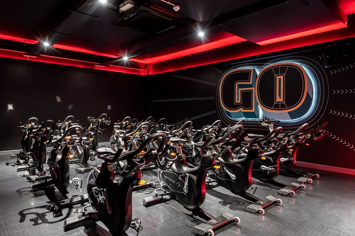 PureGym London Holloway Road: Rows of exercise bikes in a dimly lit studio with neon red lighting and "GO" signage.