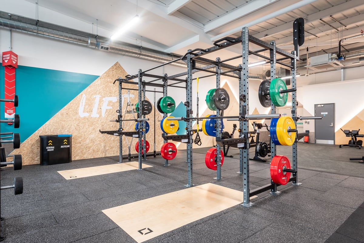 PureGym Bideford: Squat racks, colourful weight plates, rubberized flooring in a gym weightlifting area.