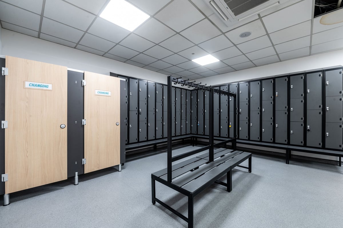 PureGym Epsom: Rows of lockers, benches, and cubicles for changing clothes in a gym changing room.