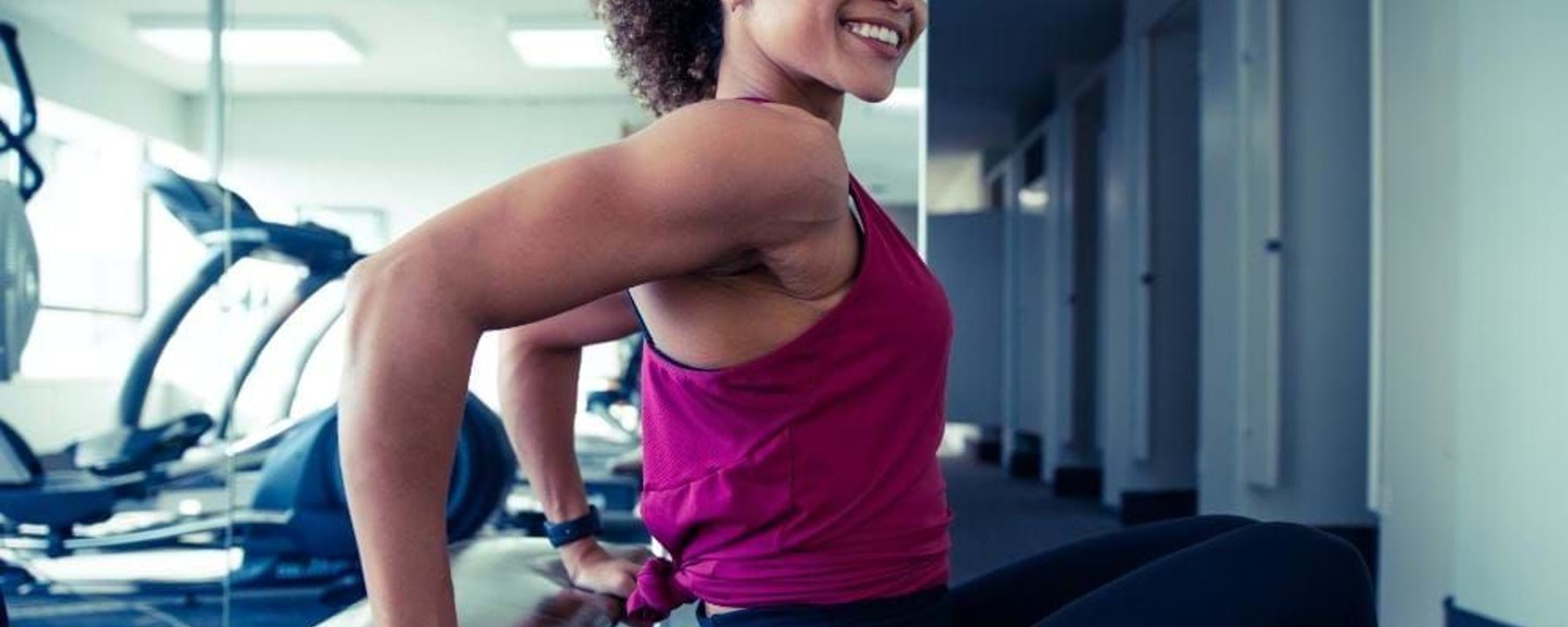 Woman in purple top doing tricep dips on bench in gym with cardio machines.