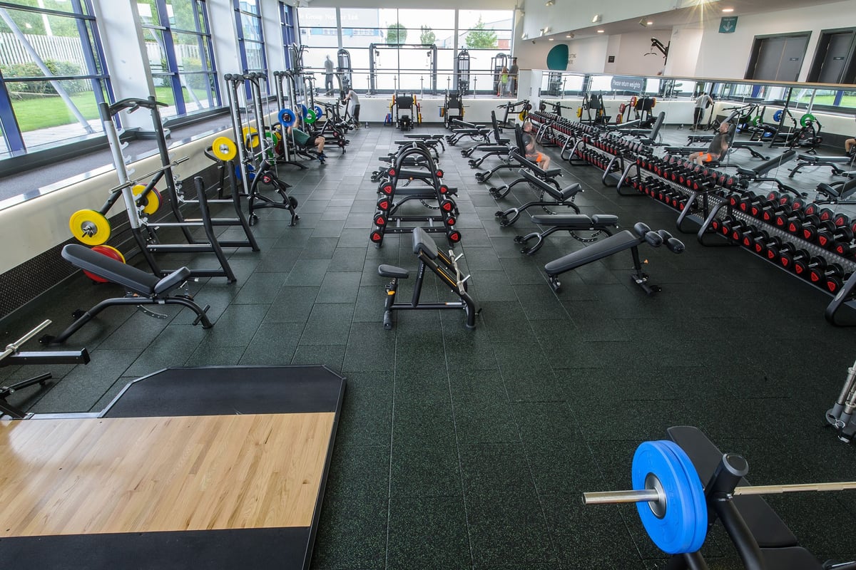 PureGym Denton: Weight racks, benches, dumbbells, rubber flooring in a bright gym space with large windows.