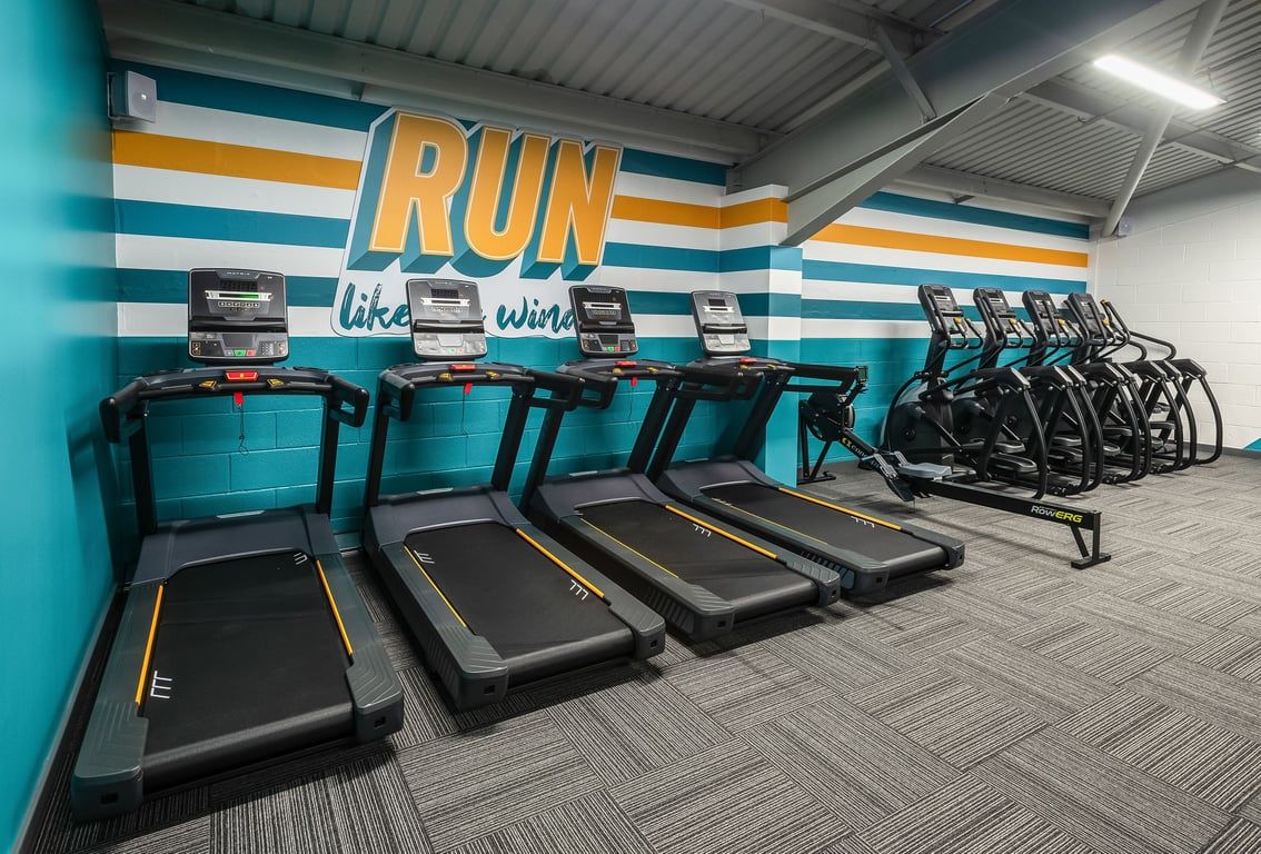 PureGym Llantrisant: Rows of treadmills alongside colourful motivational wall signage in a fitness centre.
