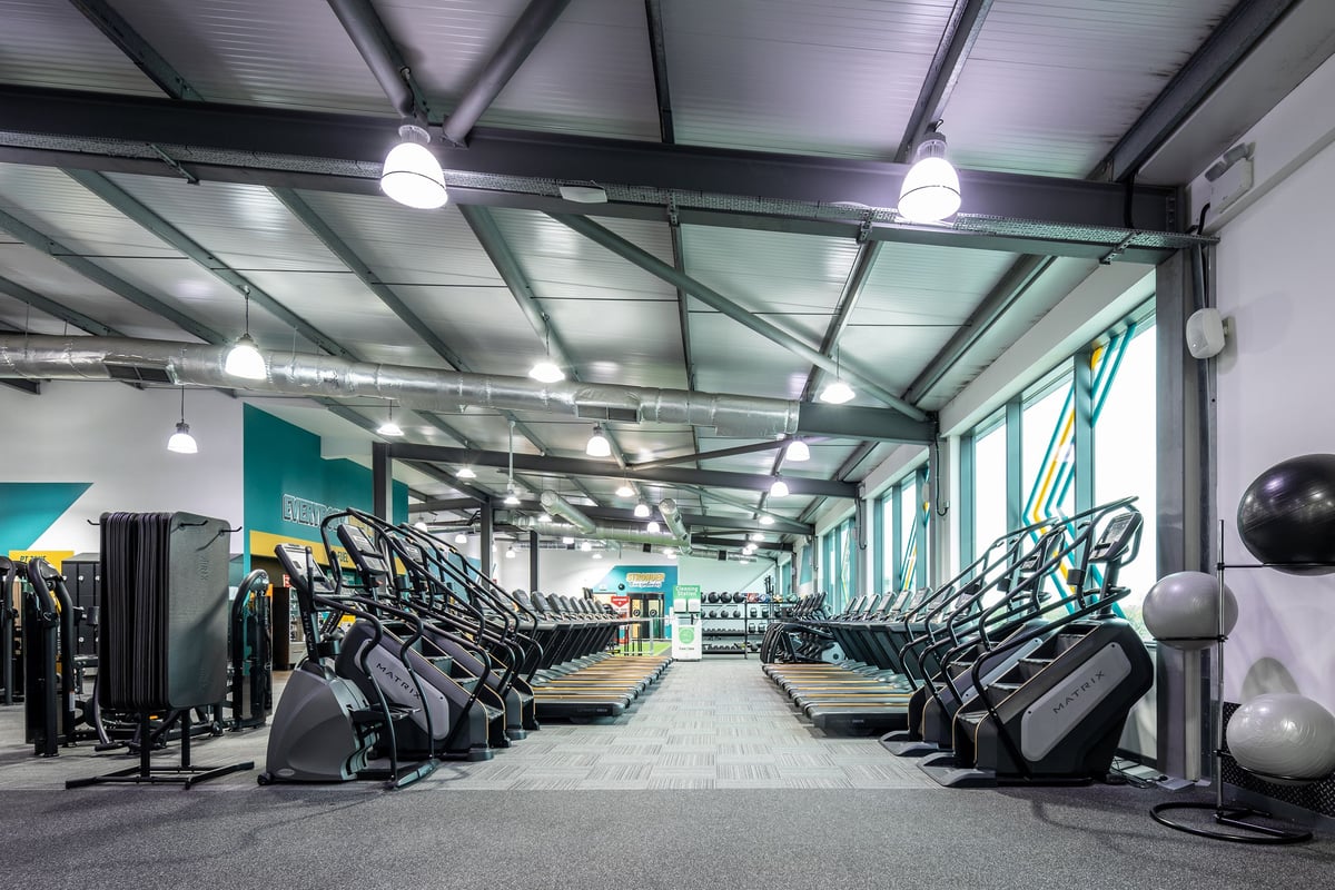 PureGym Cardiff Gate: Rows of arc trainers, treadmills, stationary bikes, and free weight equipment on rubberized flooring.
