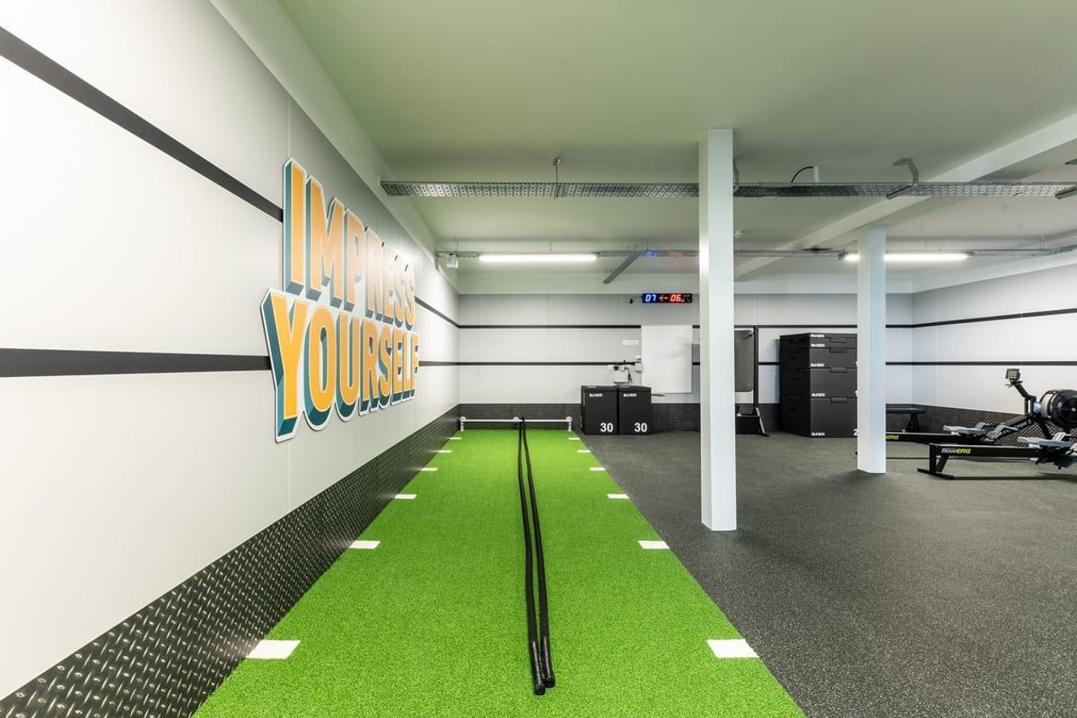 PureGym Glasgow Giffnock: Green turf, weights area, ceiling-mounted rigs in a basement-style gym interior.