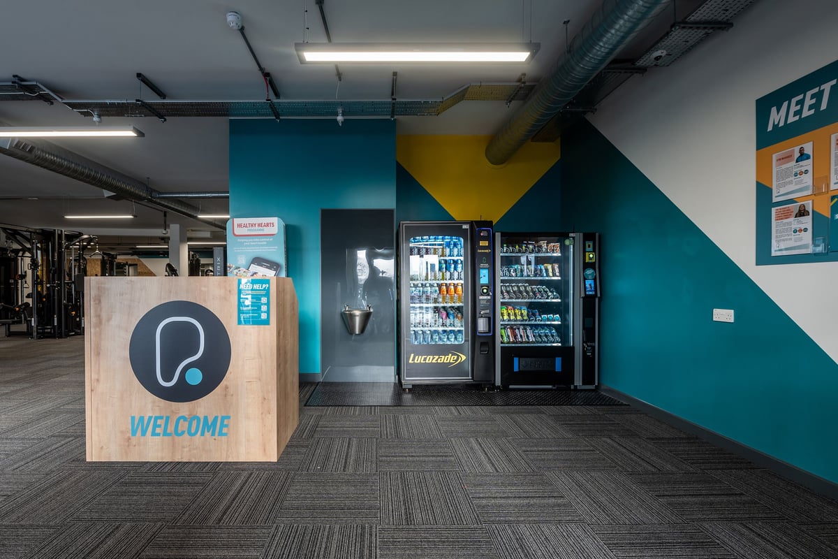 PureGym London Swanley: Vending machines, welcome sign, and bright teal and yellow accent walls.