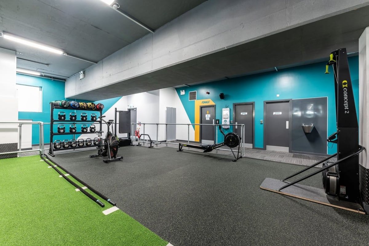 PureGym London Finsbury Park: Gym with turf area, free weights, resistance machines, and lockers along teal accent wall.
