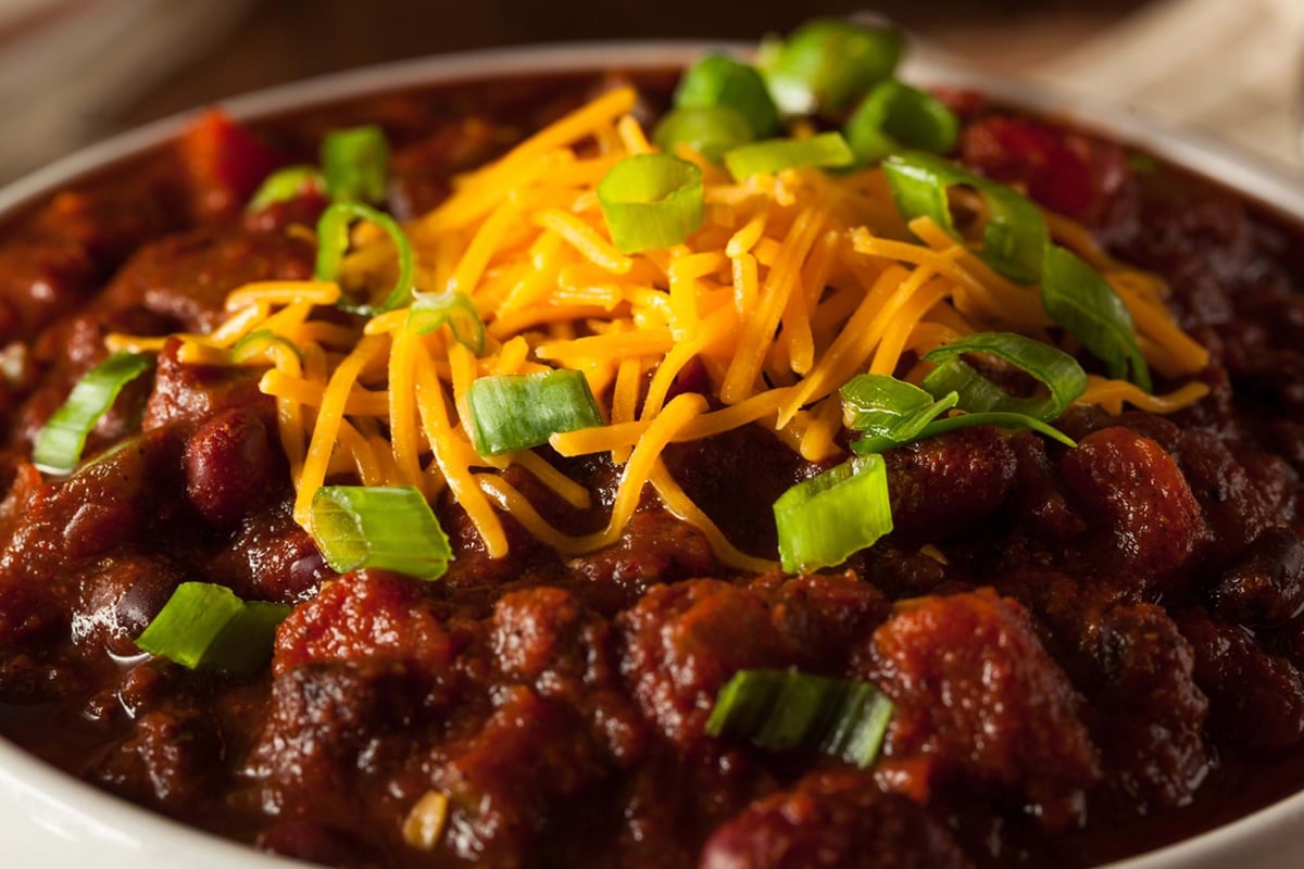 Chilli topped with shredded cheddar cheese and chopped spring onions in a bowl