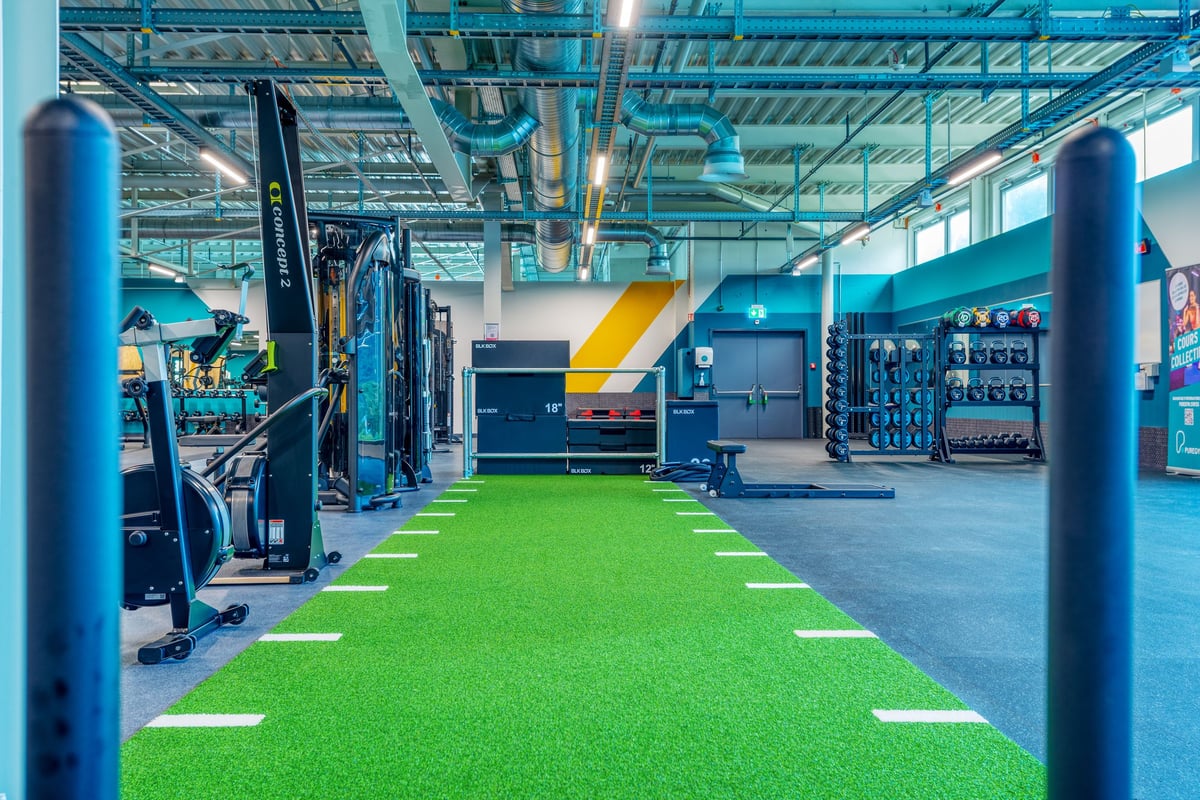 PureGym Martigny: Fitnessstudio mit Kraftgeräten, Rasenfläche, Hantelständern und Suspensionstrainern.