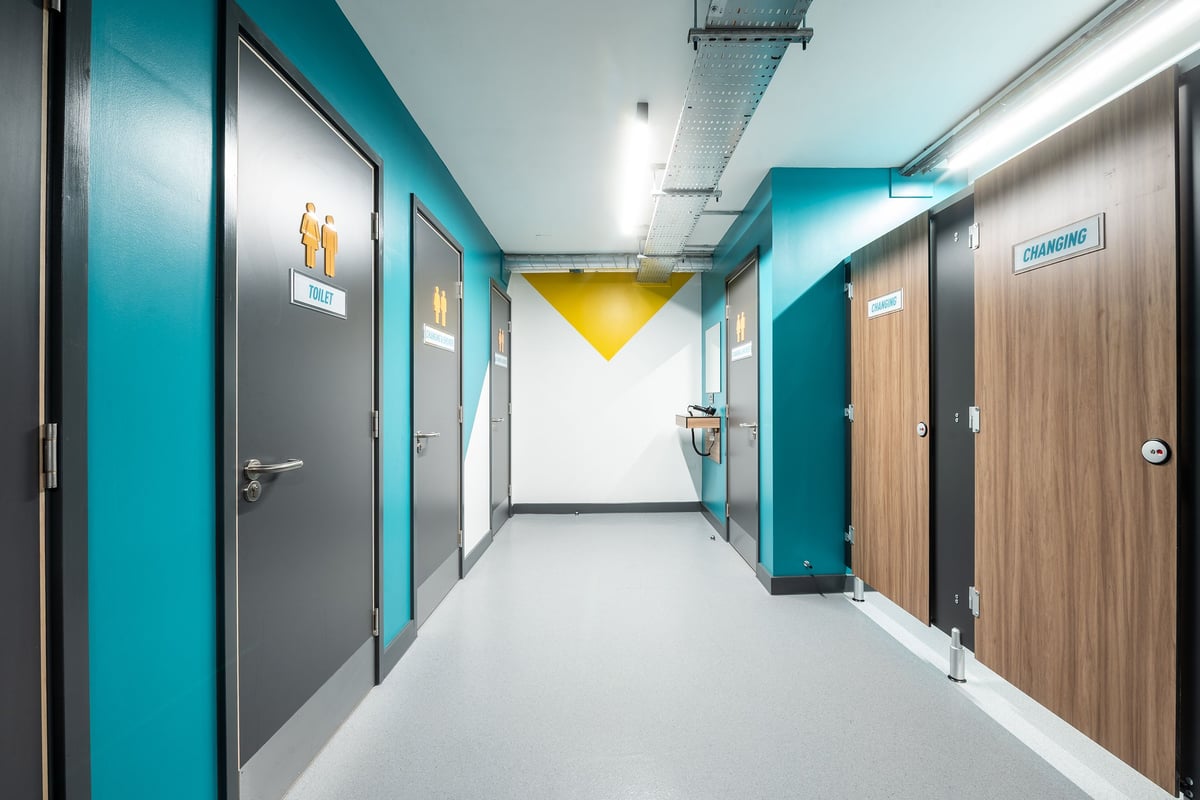 PureGym London Welling: Hallway with teal-colored walls, wooden doors, and motivational posters.