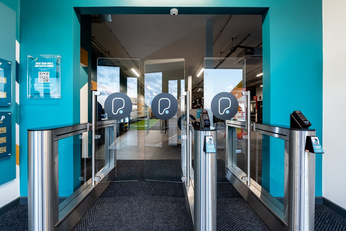 PureGym Letchworth: Turnstiles, self-service kiosks, and teal-colored entrance to fitness facility.