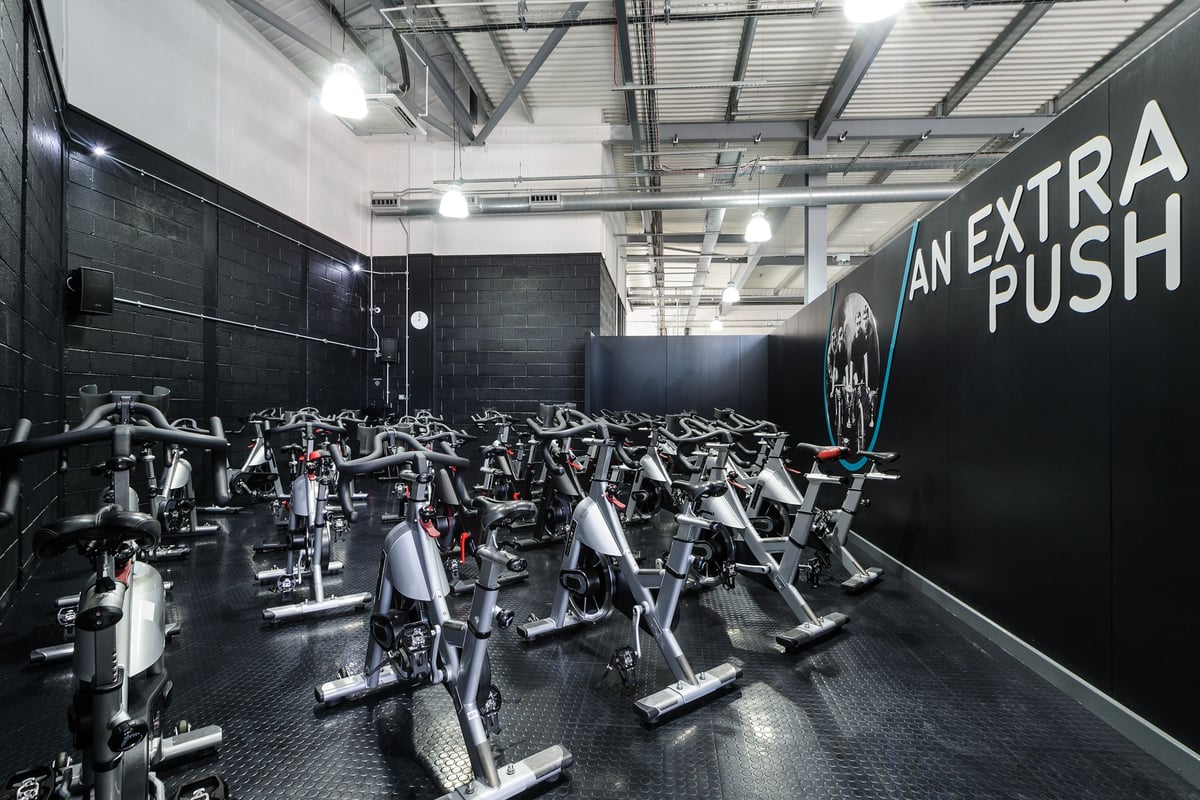 PureGym Worcester: Rows of stationary bikes inside a dimly lit fitness studio, motivational slogan on the wall.