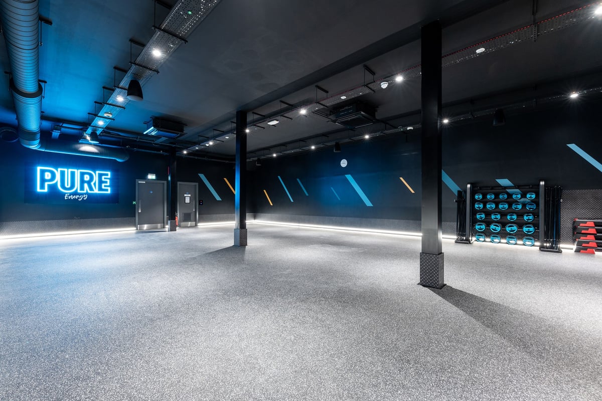 PureGym Dewsbury: Spotlights, blue-tinted interior space with electronic display board and Pure Energy branding.