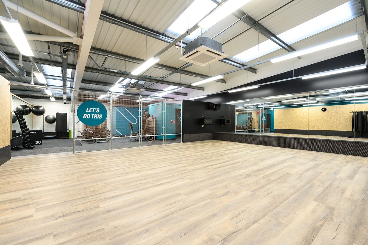 PureGym Rayleigh: Open gym space with wooden flooring, skylights, motivational signage, and workout area dividers.