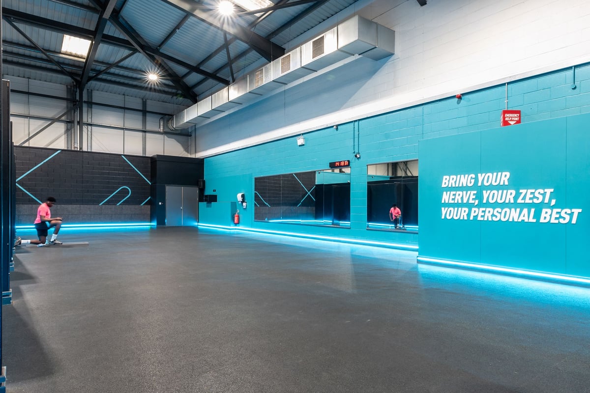 PureGym Leeds Hunslet: Boxing ring area, punching bags suspended, teal accent walls with motivational slogan.