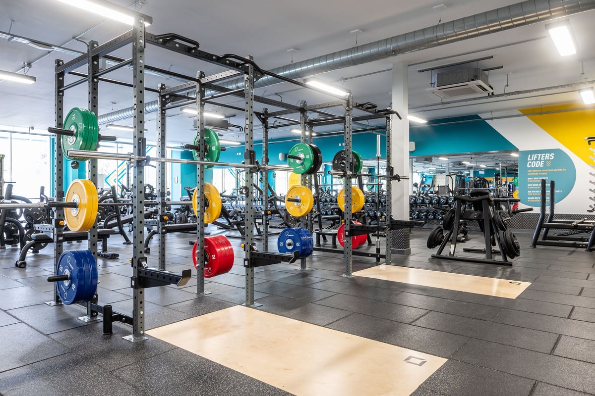 PureGym Wirral Bidston Moss: Row of squat racks with colourful weight plates, free weights, mirrors, rubberised flooring.