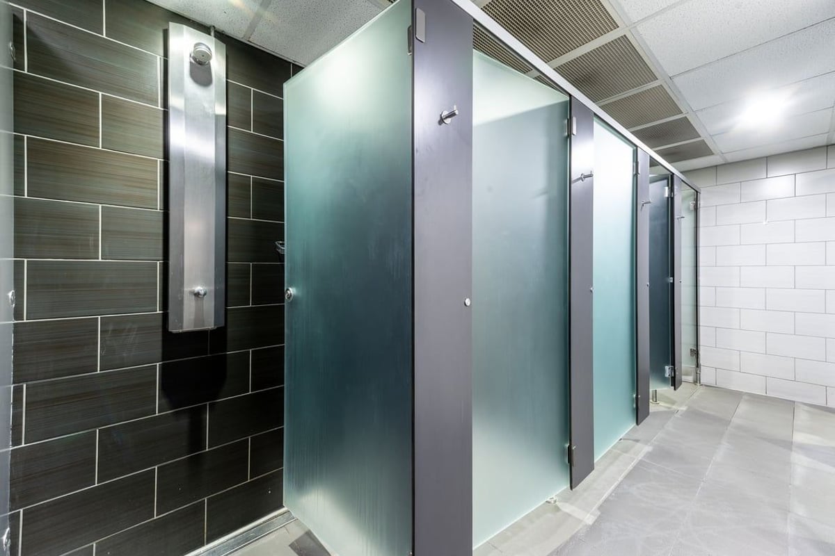 PureGym Northolt: Rows of shower stalls with frosted glass doors and tiled walls.
