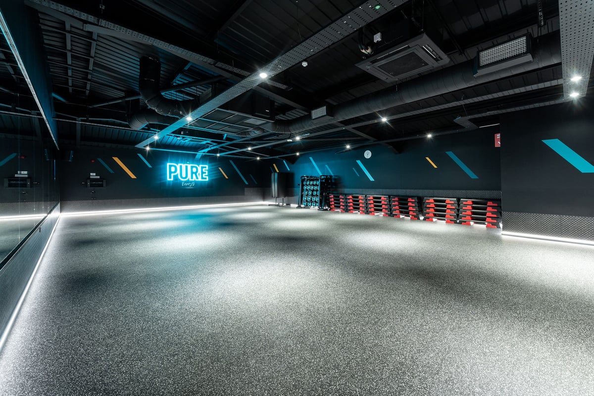 PureGym Macclesfield Silk Road: Red spin bikes line one wall in a futuristic studio with neon lighting and grey floors.