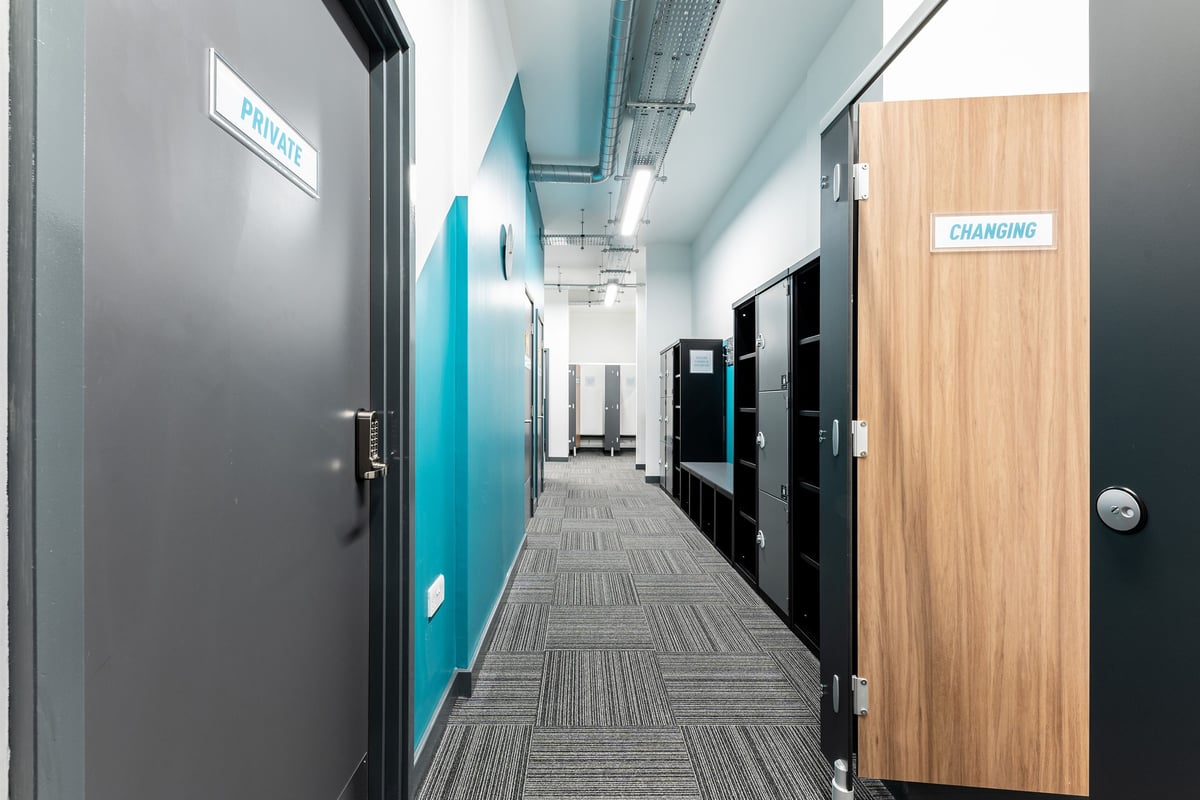 PureGym London Palmers Green: Changing rooms with wooden doors and blue signage along a corridor.