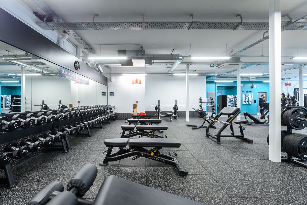 PureGym Barnstaple: Rows of weight benches, dumbbell racks, and rubberized flooring in a gym setting.