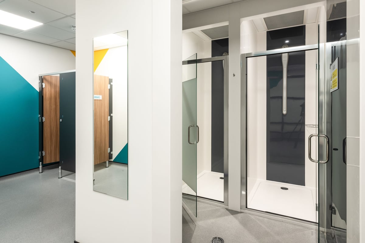 PureGym Llantrisant: Shower stalls, cubicles with wooden doors, frosted glass partitions, and tiled floors.