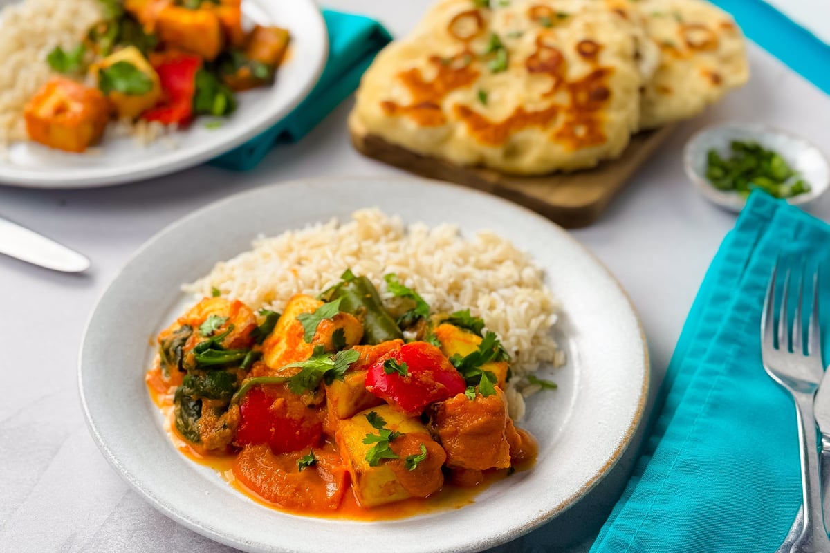 Plates of vegetable curry with rice and naan bread on a white table with turquoise napkins