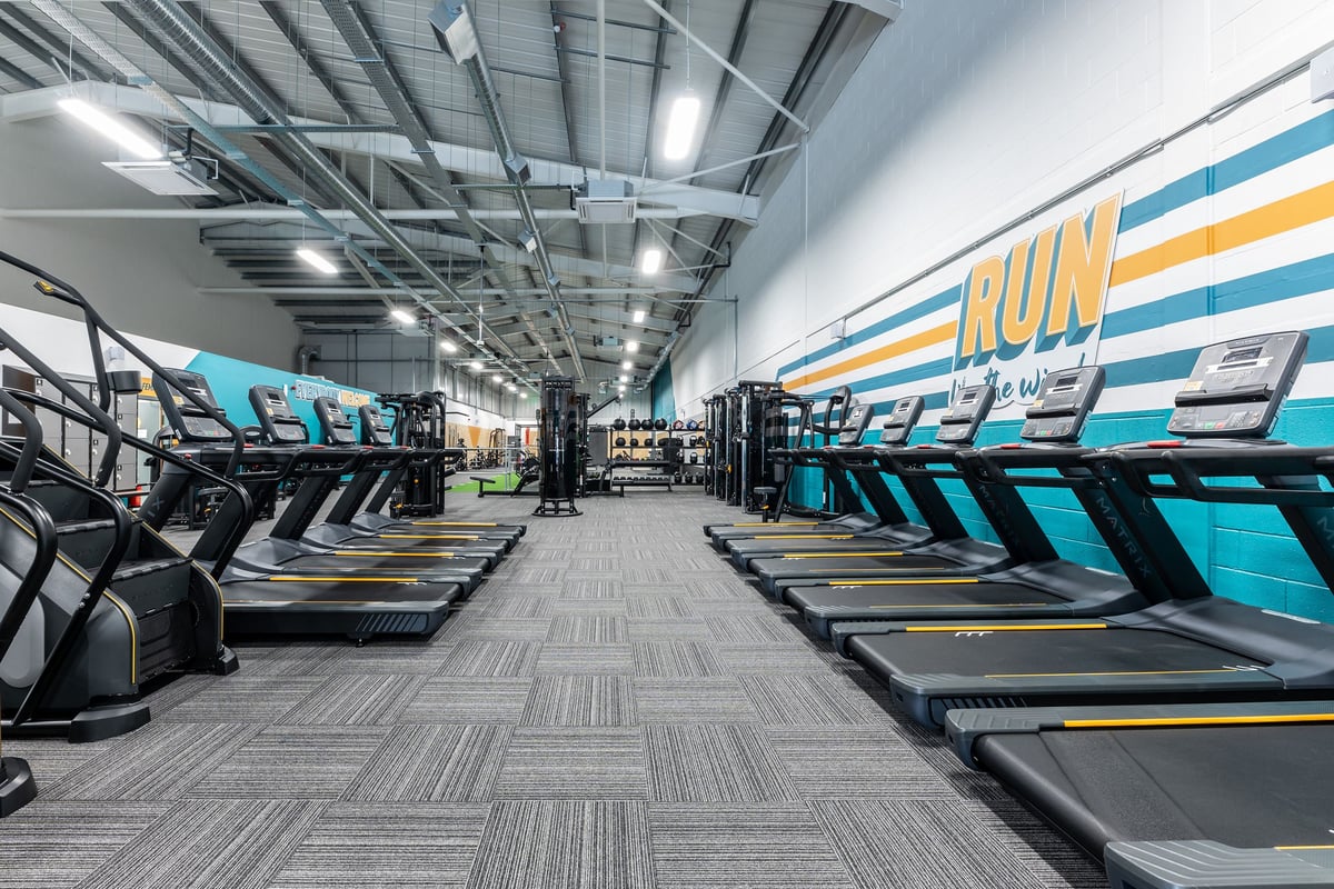 PureGym Byfleet: Rows of treadmills, bright lighting, and wall graphics featuring the word "RUN" in a gym setting.