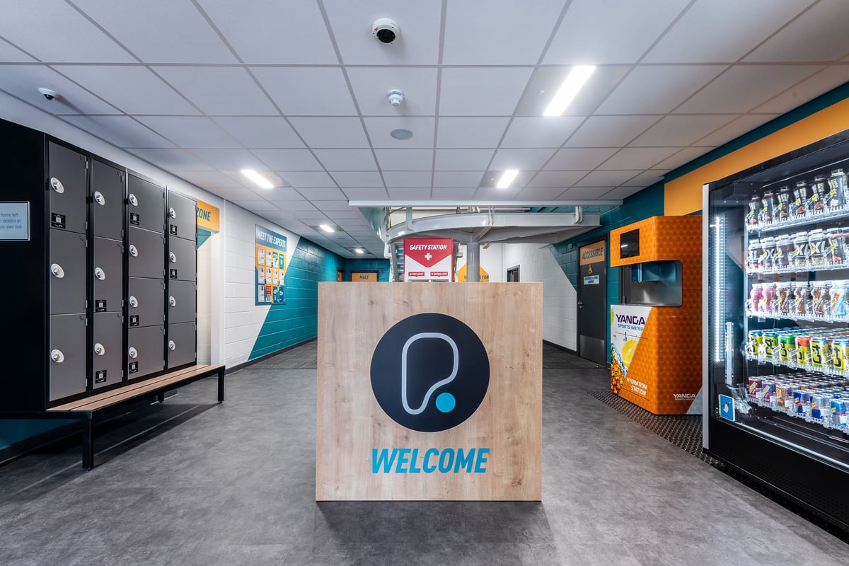 PureGym Sheffield Crystal Peaks: Rows of lockers, vending machines, welcome sign, and teal accent walls.