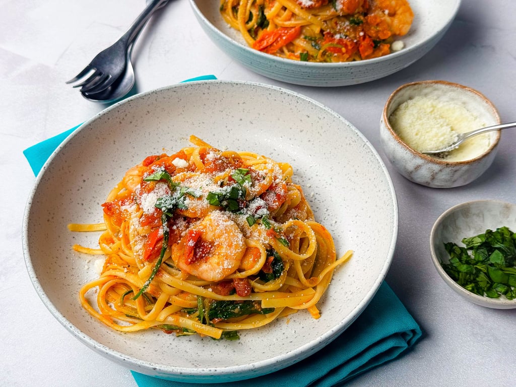 Linguine pasta with shrimp, tomato sauce, spinach, and grated cheese in bowls.