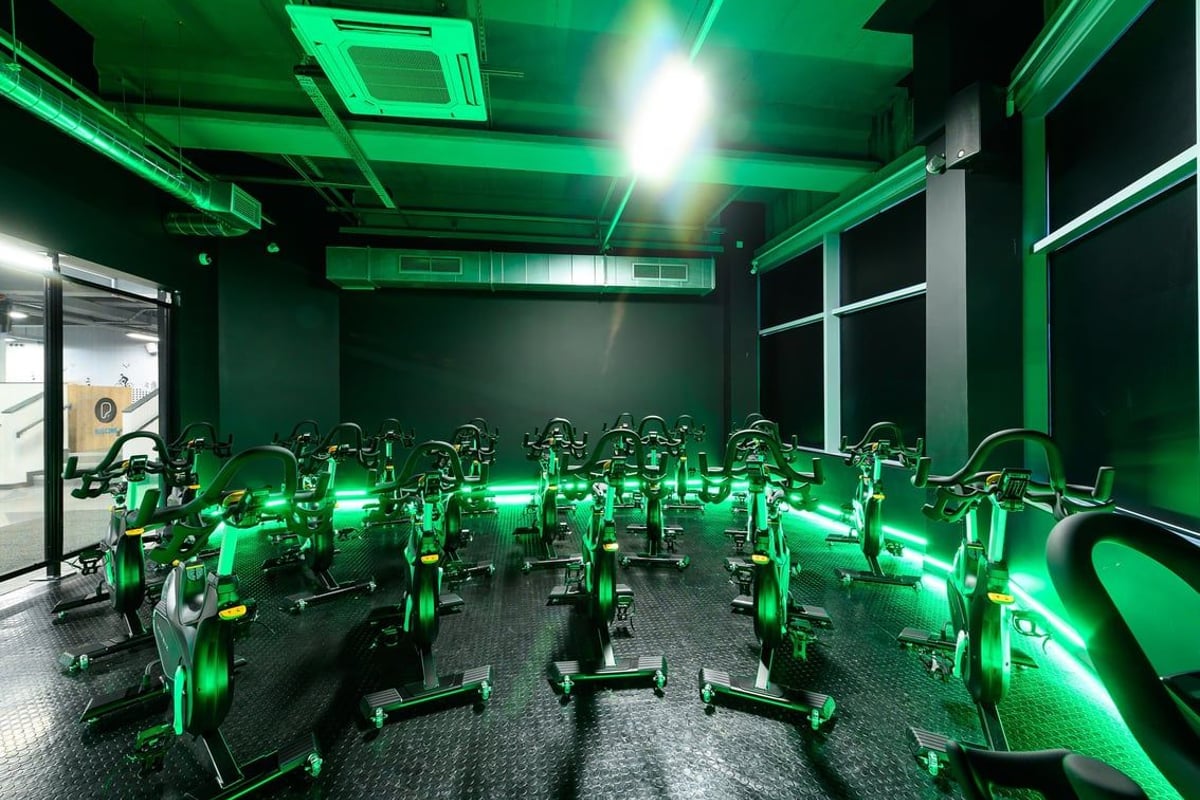 PureGym Leeds City Centre North: Rows of stationary bikes illuminated by neon green lighting inside a fitness studio.