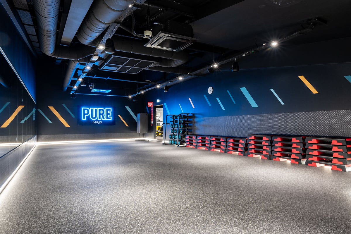 PureGym Kettering: Auditorium-style seating, glossy flooring, and neon "PURE" signage in blue hues.