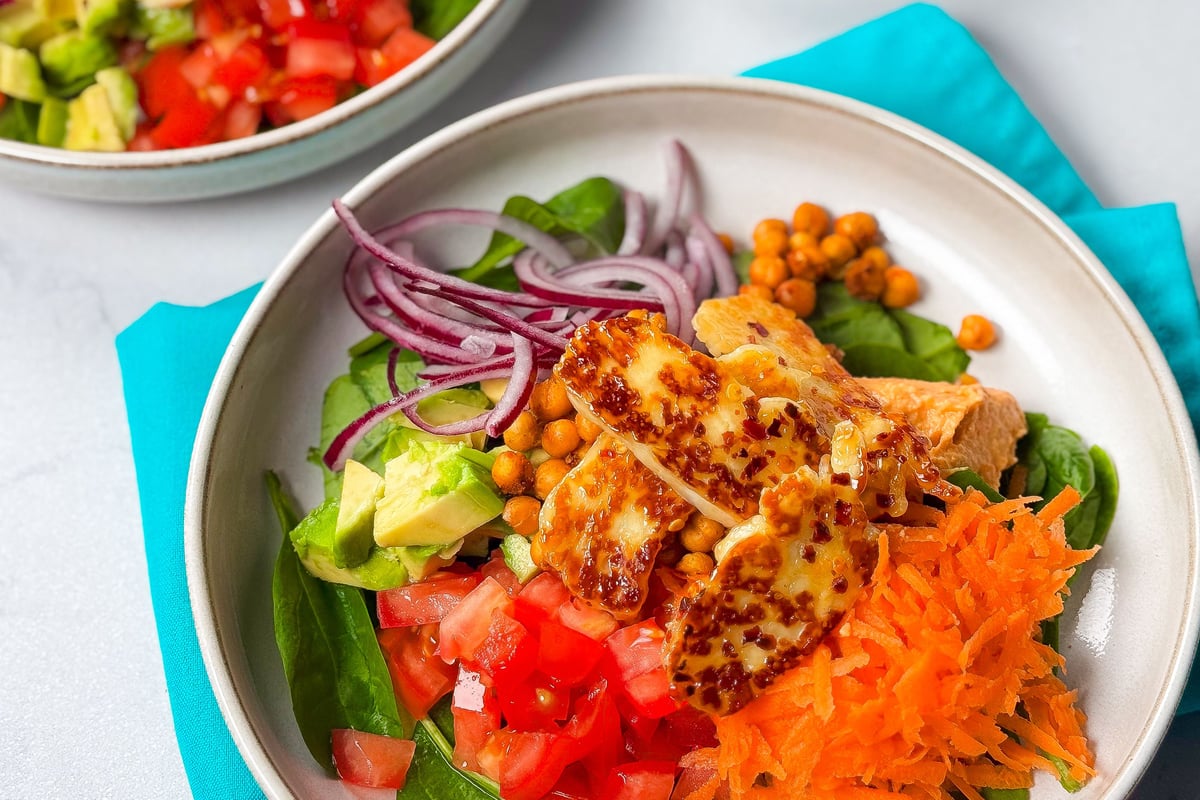 Grilled halloumi slices over salad bowl with chickpeas, vegetables and grated carrot