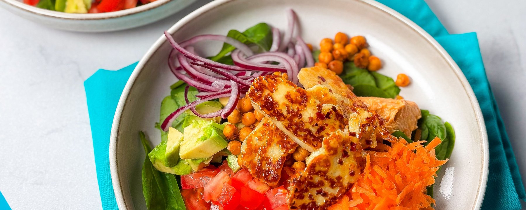 Grilled halloumi slices over salad bowl with chickpeas, vegetables and grated carrot